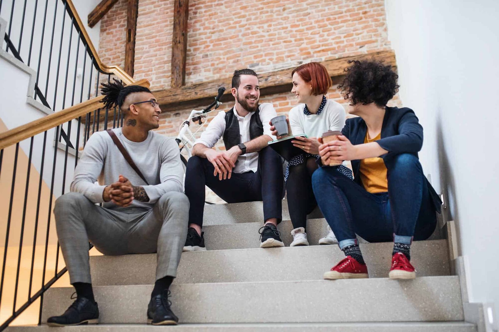 Group of young businesspeople sitting on stairs indoors, talking